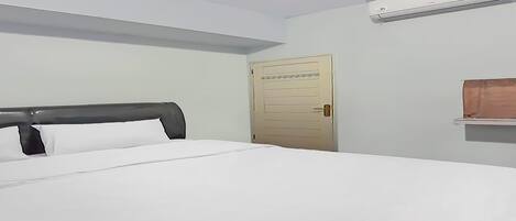 A hotel room with a bed, a door, and an air conditioning unit.