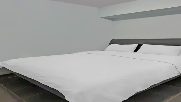 A neatly made bed in a room with white walls and a dark floor.
