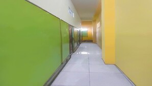 A long, narrow hallway with green and yellow walls, tiled floor, and doors on the left.