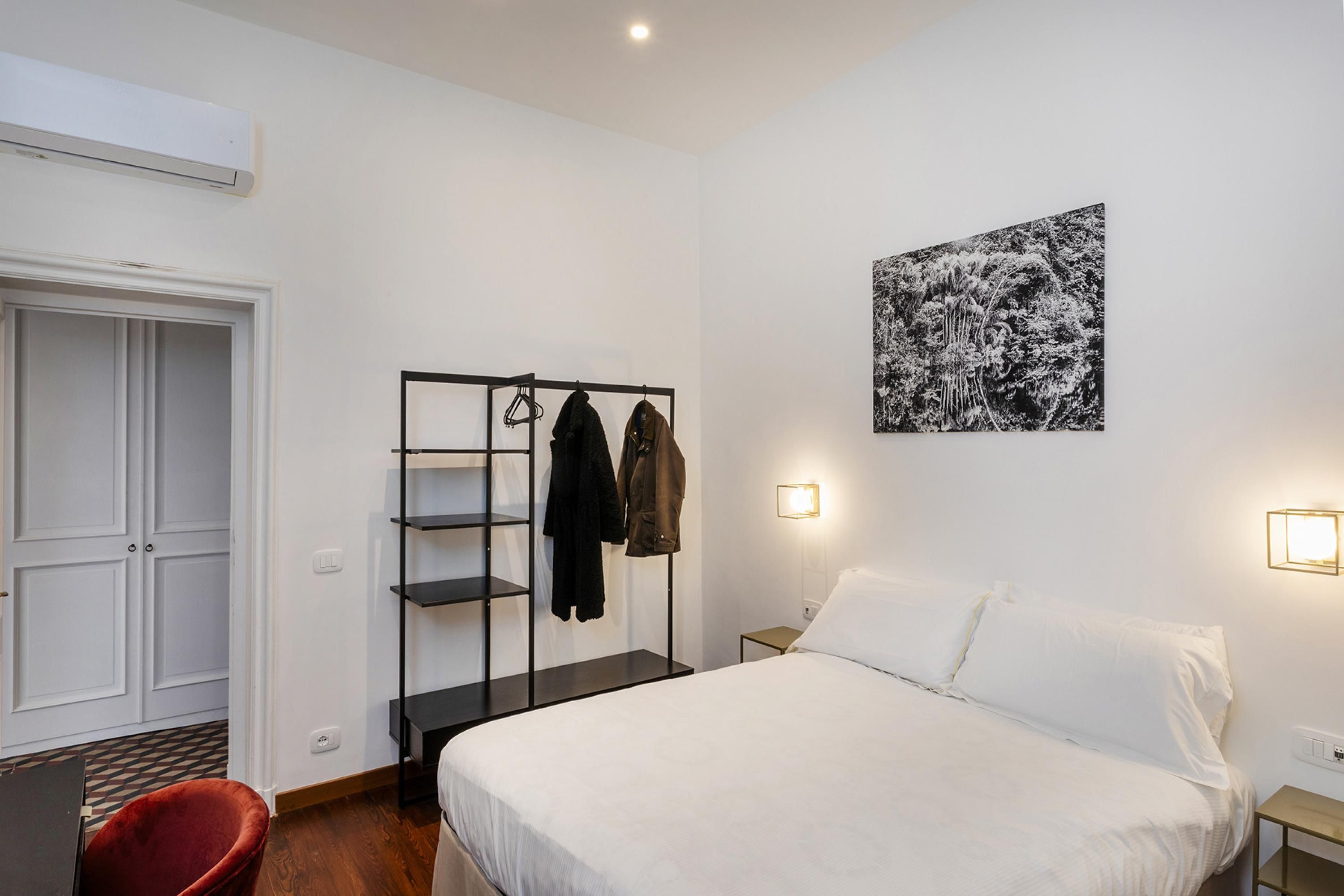 Ein Schlafzimmer mit einem Bett, einem Kleiderschrank, einem Kleiderständer und einem an der Wand hängenden Bild.