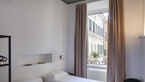 A hotel room with two beds, a window with curtains, a radiator, and a view of buildings outside. - La Residenza Delle Vigne by Wonderful Italy (Genoa)
