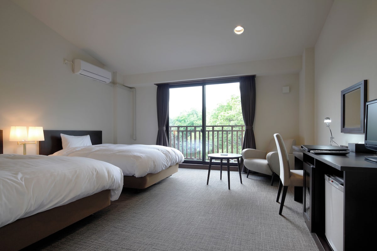 Une chambre d’hôtel avec deux lits, un bureau avec une chaise, une télévision et une fenêtre avec des rideaux.