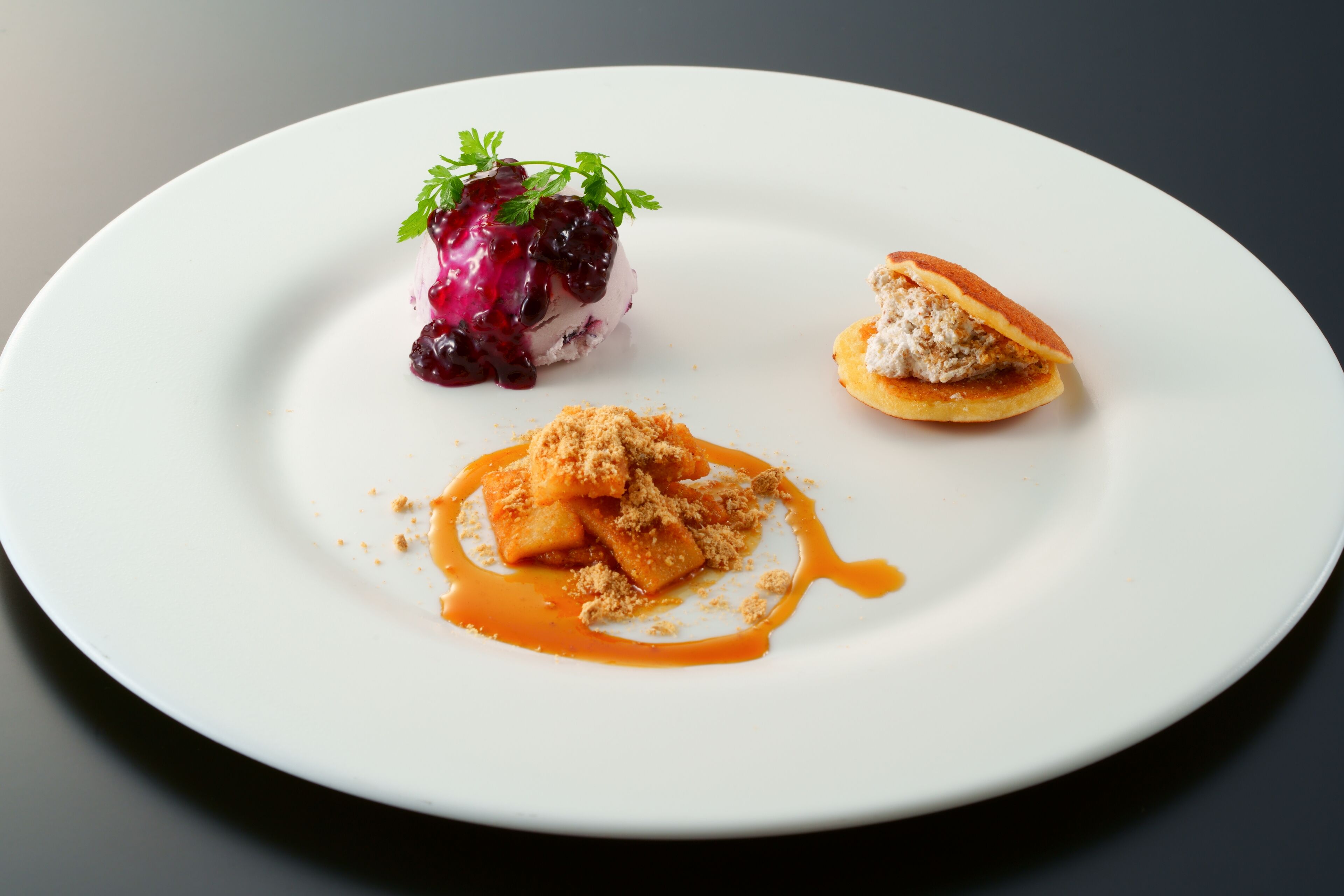 A white plate with three food items: a dessert with berries and a sauce, a pastry with a crumb topping, and a small piece of bread with a creamy filling.