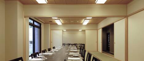 A conference room with a long table set for a meeting, equipped with chairs and tables, and a large window on one side.