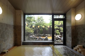 Una tradizionale onsen giapponese con interni in pietra, vista su un giardino curato e soffitto in legno.
