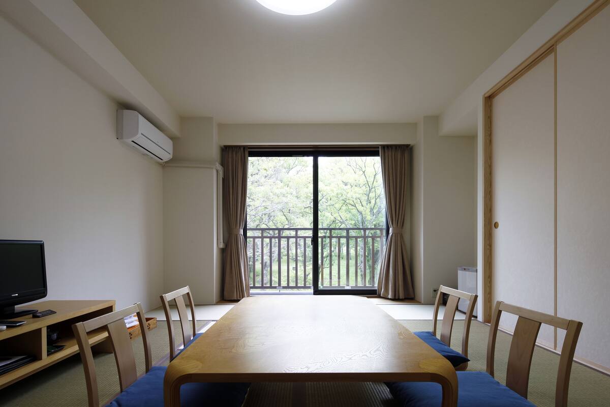Une pièce comprenant une table en bois, des chaises, un téléviseur et une porte-fenêtre coulissante donnant sur un balcon.