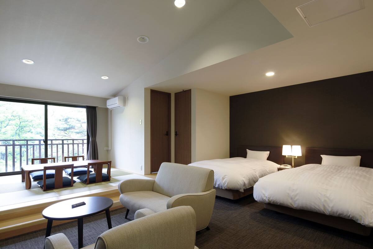 Une chambre d’hôtel avec deux lits, un canapé, une petite table et un balcon donnant sur la verdure.