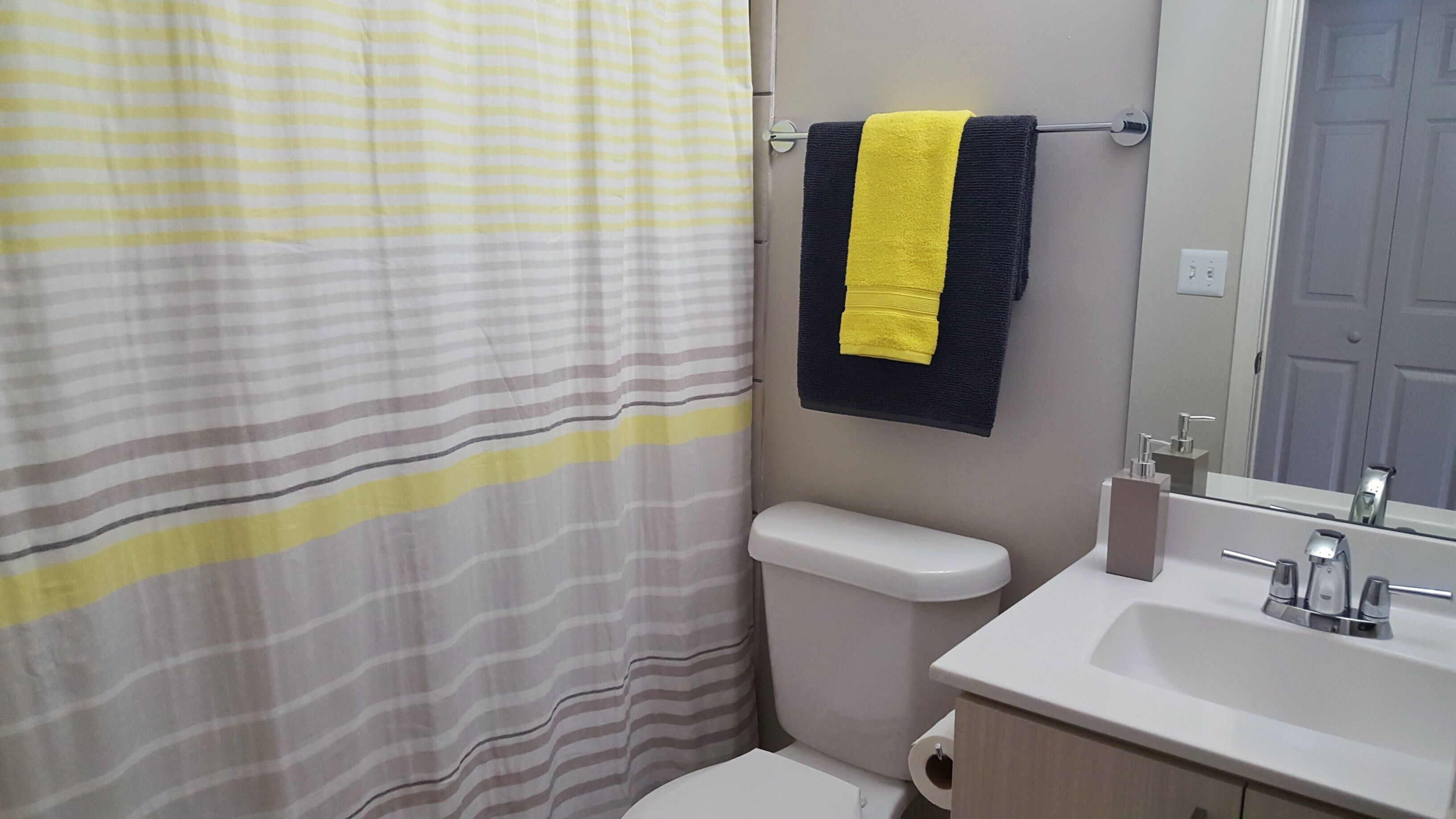 Un baño con cortina de ducha a rayas, un inodoro, un lavabo y un perchero con una toalla amarilla y negra.