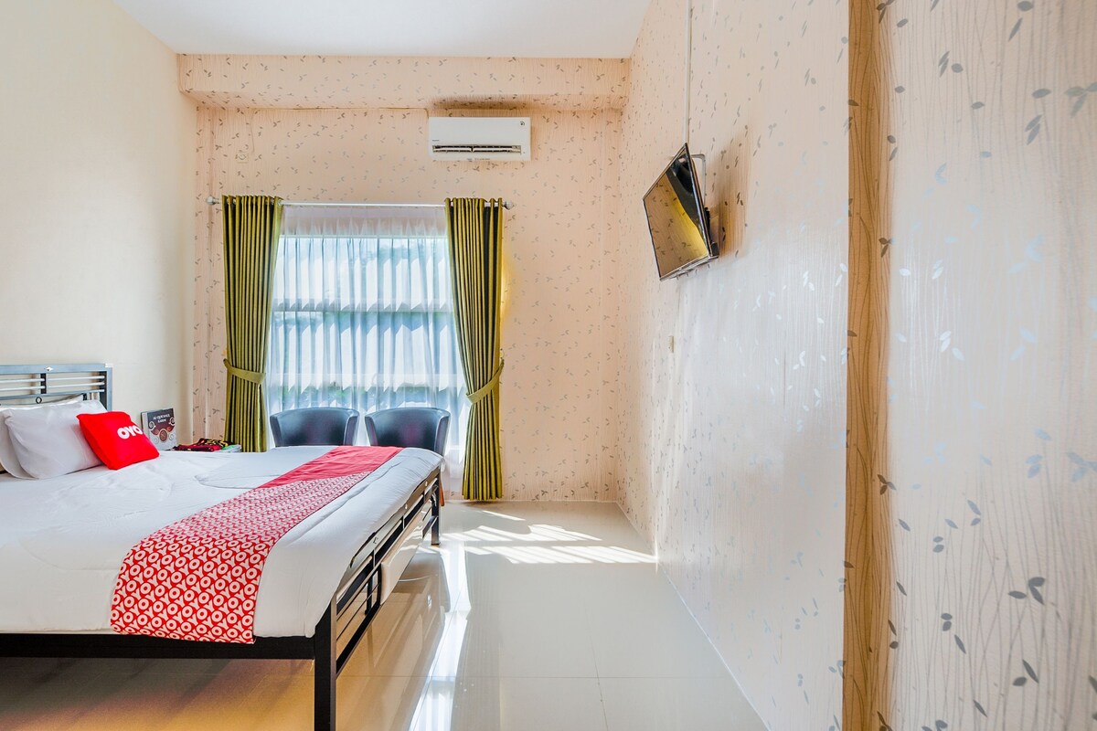 A hotel room with a bed, a TV mounted on the wall, and a window with curtains.