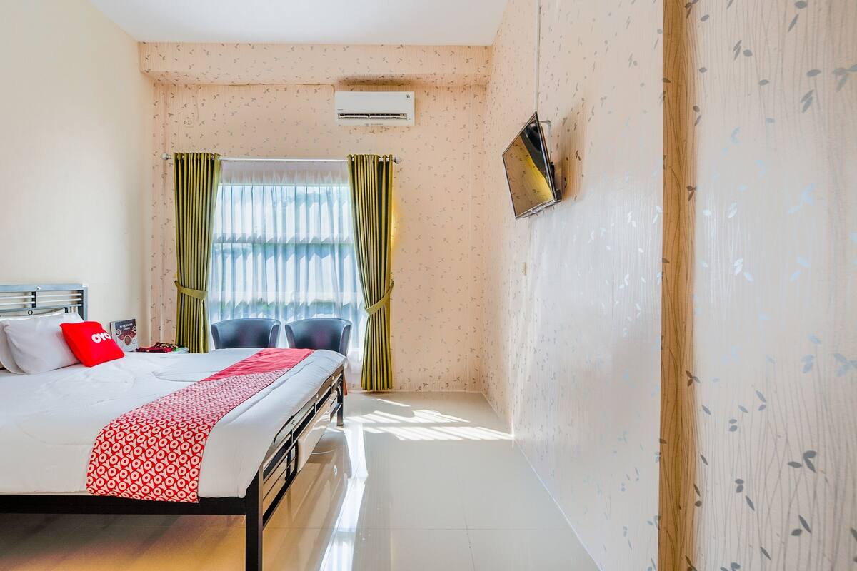Une chambre d’hôtel avec un lit, un téléviseur fixé au mur et une fenêtre avec des rideaux.