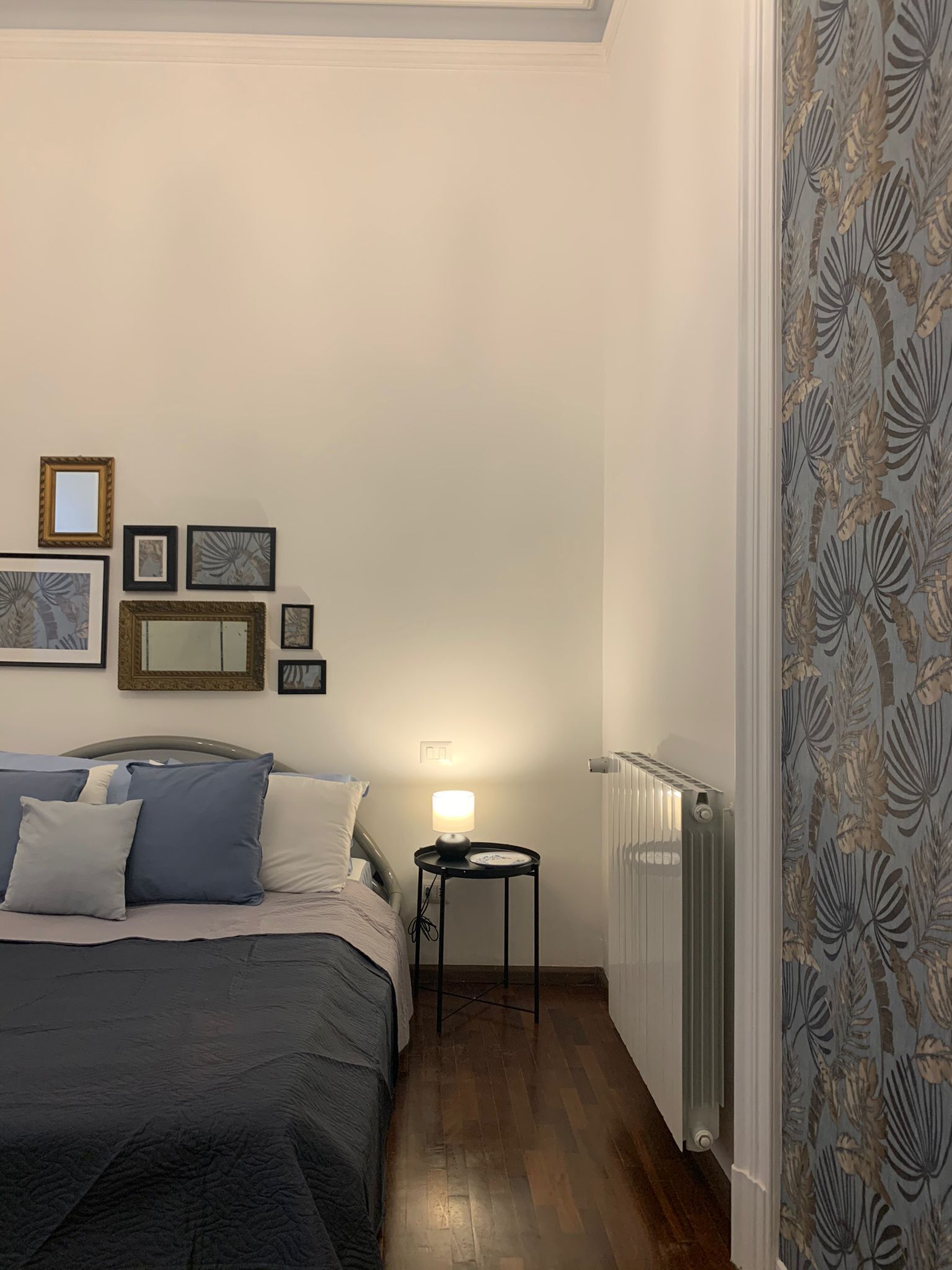 A bedroom with a bed, bedside table, lamp, and wall-mounted pictures.
