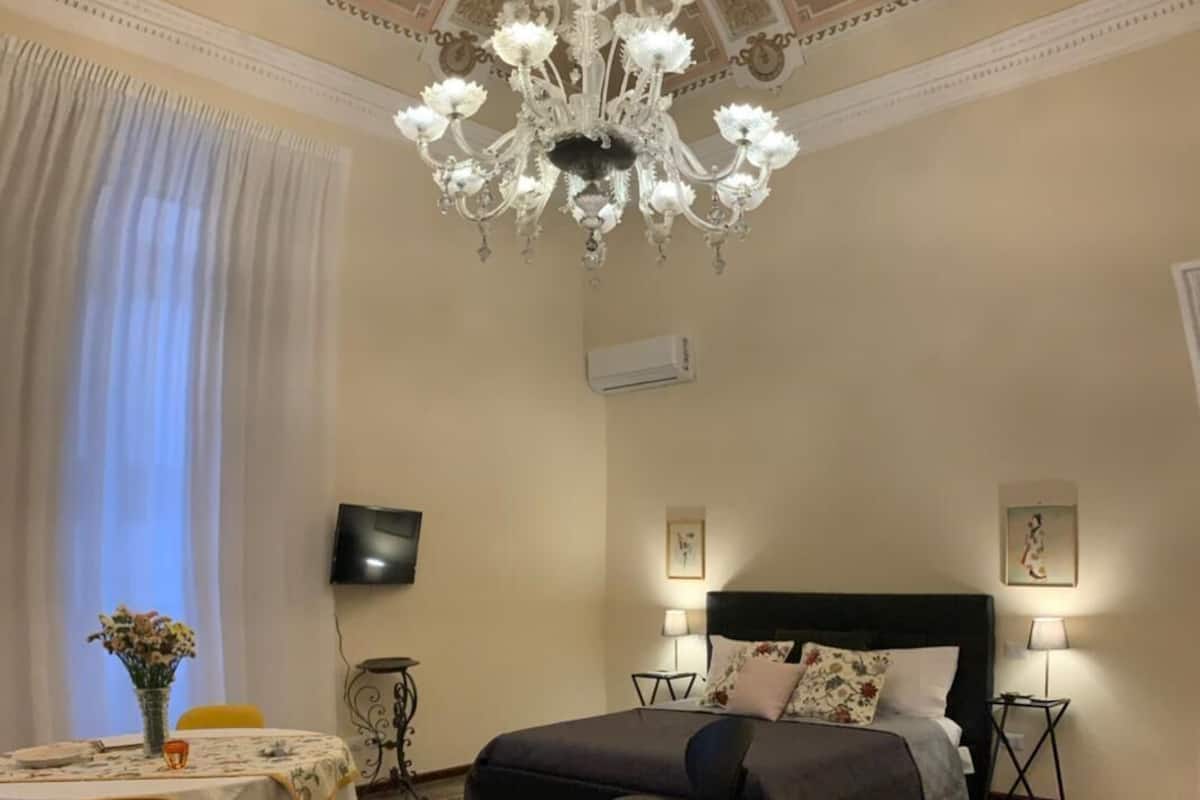 Un dormitorio con una cama grande, una araña de cristal, una mesa de comedor con sillas y una alfombra estampada.