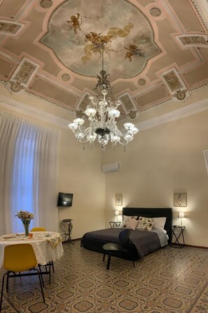 Ein Schlafzimmer mit einem großen Bett, einer Chandelüster, einem Esstisch mit Stühlen und einem gemusterten Teppich.