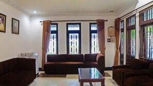 A living room with a sofa set, a glass coffee table, and large windows with curtains. - Hotel O Medan City Near Sun Plaza Formerly 99 Residence (Medan)