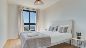 Una camera da letto con un letto grande, un comodino con una lampada e vista sul mare attraverso una finestra.