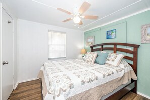 Un dormitorio con estructura de cama de madera, ventilador de techo y ventana con persianas.