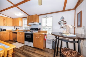 Cocina compacta con armarios de madera, estufa y un pequeño comedor con mesa y sillas.
