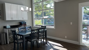 A modern kitchen with white cabinets, a black countertop, and a dining area with four chairs. - Walk to the Strip! Calm Cove Swimming, Sun Decks & Prime Lake Location (Lake Ozark)