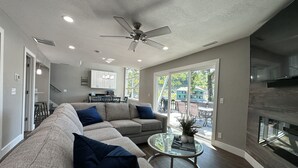 A modern living room with a sectional sofa, a glass coffee table, and a ceiling fan. - Walk to the Strip! Calm Cove Swimming, Sun Decks & Prime Lake Location (Lake Ozark)