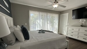A bedroom with a bed, a nightstand, a dresser, a ceiling fan, and a TV mounted on the wall. - Walk to the Strip! Calm Cove Swimming, Sun Decks & Prime Lake Location (Lake Ozark)