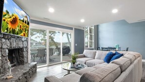 Ein modernes Wohnzimmer mit Kamin aus Stein, einem großen Fenster und einem grauen Sofa mit blauen Kissen.