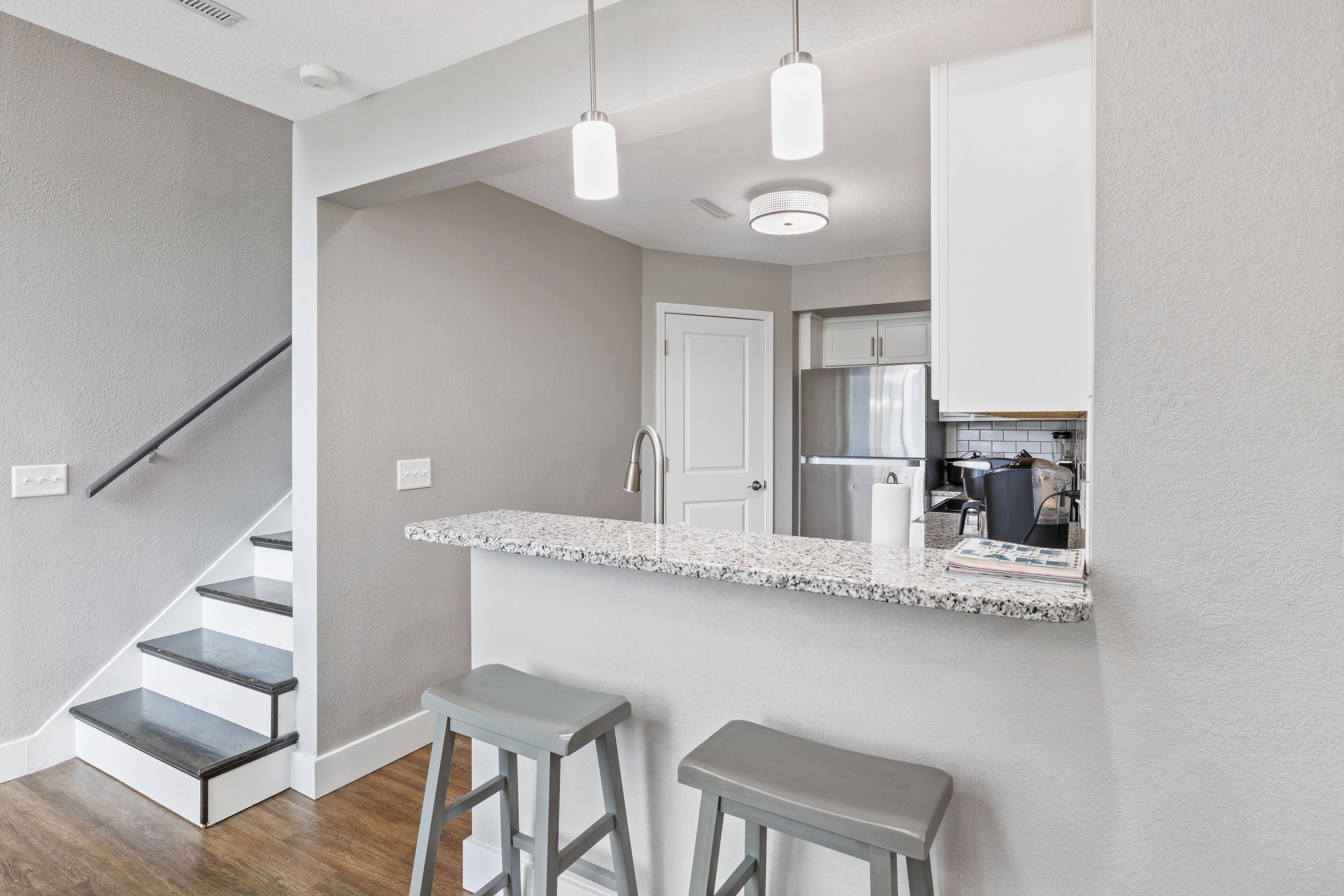 A modern kitchen with a white countertop, stainless steel appliances, and a bar area with stools.