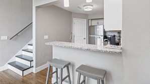 A modern kitchen with a white countertop, stainless steel appliances, and a bar area with stools.