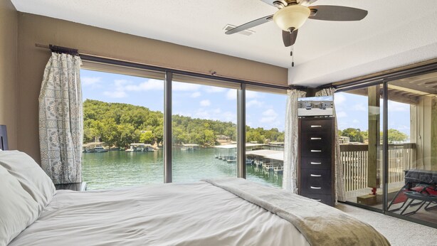A bedroom with a large bed, a ceiling fan, and a view of a lake with boats. - Stunning Views, Inviting Pools, and Endless Fun! (Osage Beach)