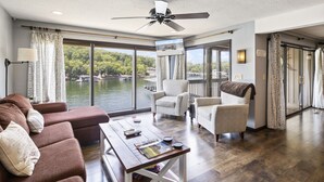 A spacious living area with a large window overlooking a body of water, furnished with a brown sofa, a white armchair, and a wooden coffee table. - Stunning Views, Inviting Pools, and Endless Fun! (Osage Beach)