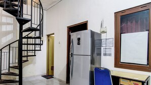 A compact kitchen with a refrigerator, a blue chair, and a wooden cabinet. - Super OYO 92511 Griya Dias  Syariah (Yogyakarta)