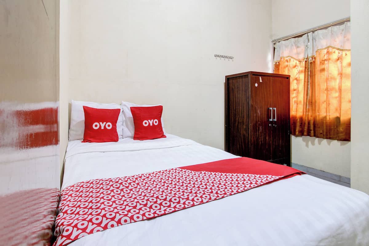 Ein ordentlich bezogenes Bett mit einer roten und weißen Tagesdecke und zwei Kissen mit dem Schriftzug „OYO“.