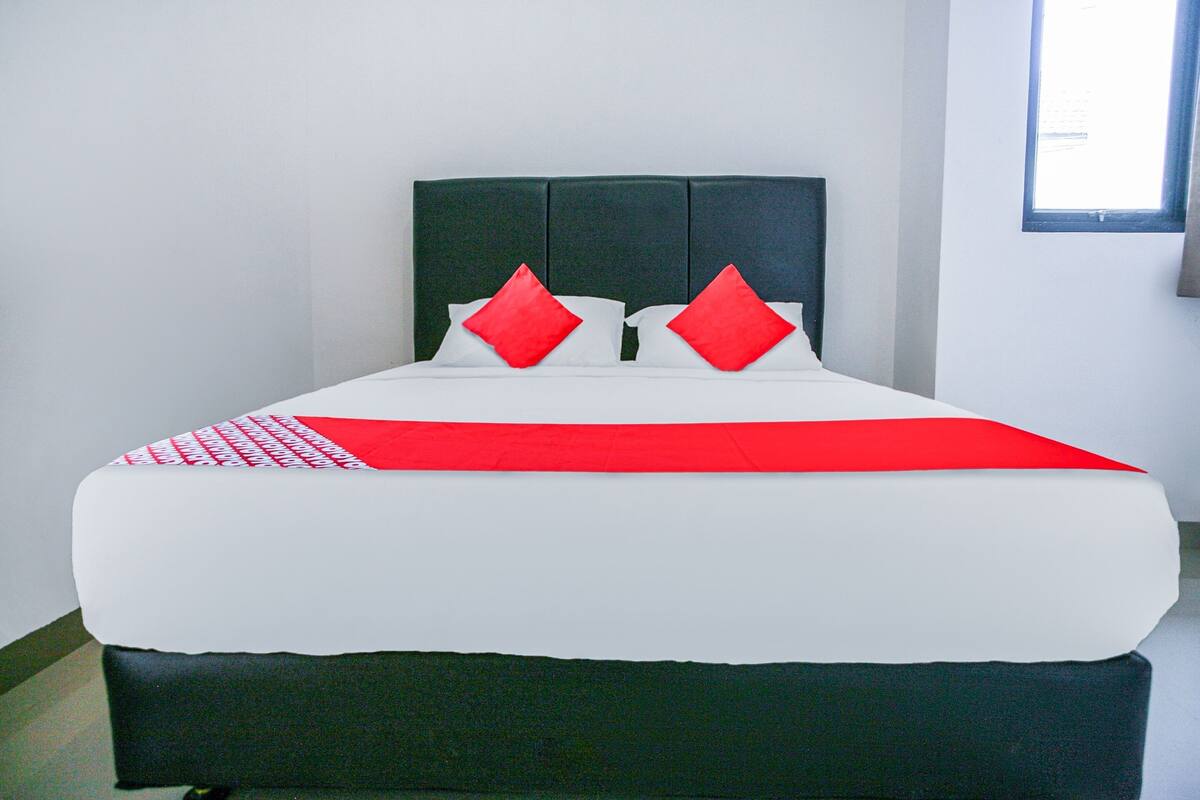 Un lit avec une couvre-lit blanche et rouge, deux oreillers rouges et une tête de lit noire.
