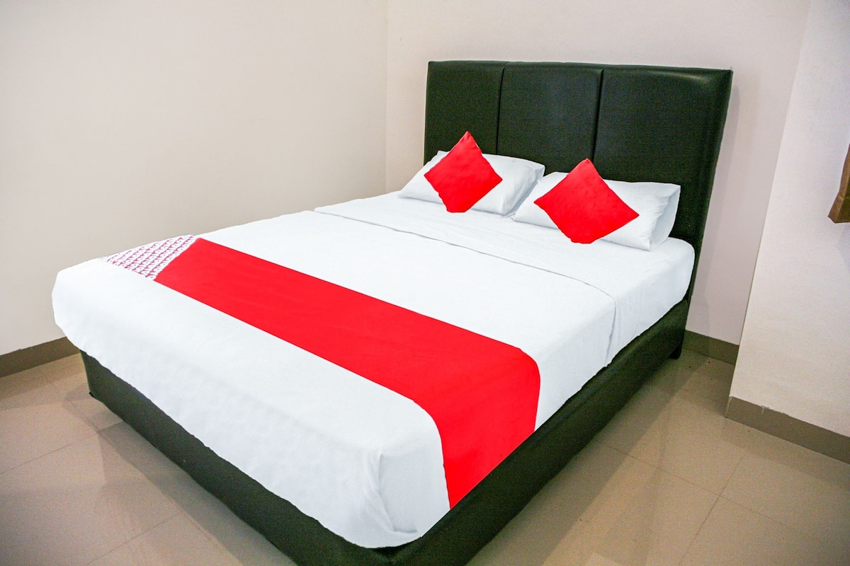 Un lit avec une couvre-lit blanche et rouge, deux oreillers rouges et une tête de lit recouverte d’un tissu vert.