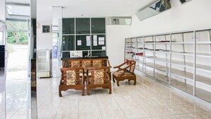 Una habitación con suelo de baldosas, una mesa de madera con sillas, una ventana con papeles y una estantería con compartimentos etiquetados.