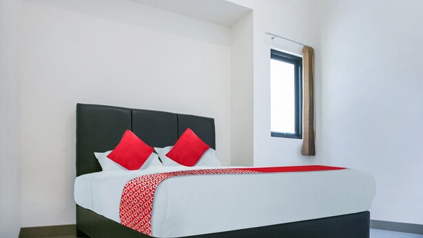 Una cama bien tendida con una colcha de cuadros rojos y blancos, un cabecero oscuro y dos almohadas rojas.