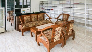 Una habitación con sofá de madera, una mesita y una encimera con una computadora. Se observan estantes con diversos objetos al fondo.