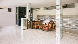 Una habitación amplia con suelo de baldosas, un refrigerador, una mesa de madera con sillas y una estantería con archivadores.