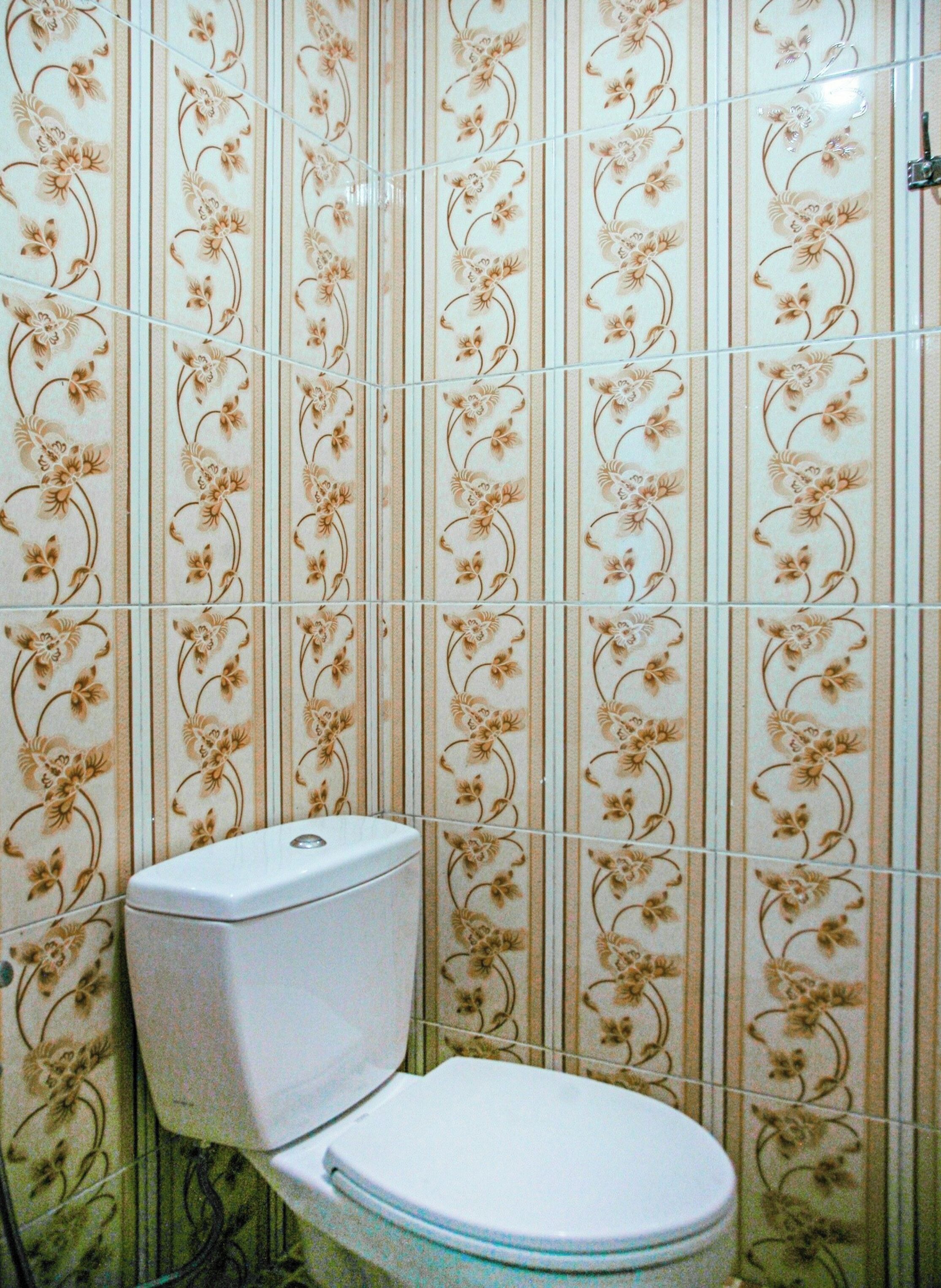 A bathroom with a toilet and a wall with floral patterned tiles.