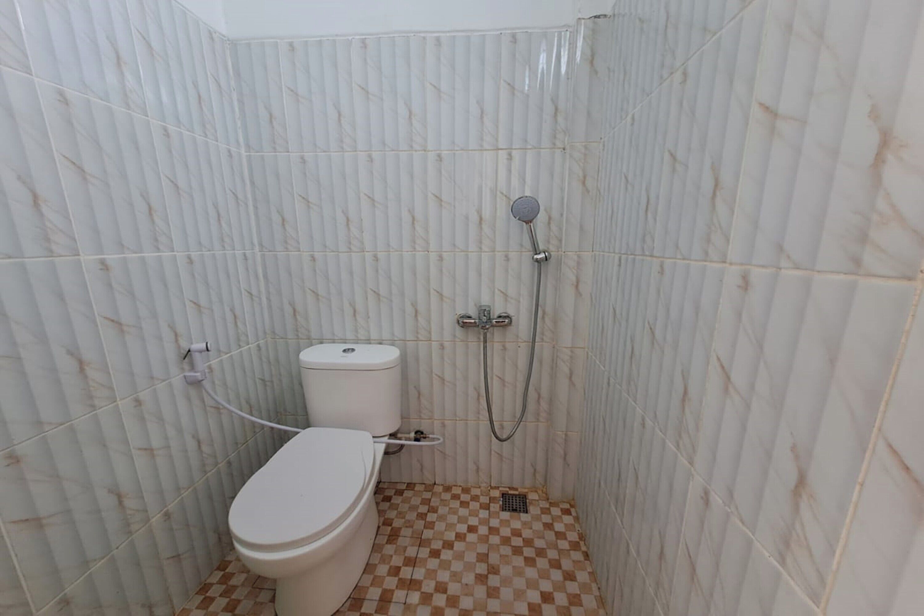 Une petite salle de bain avec des toilettes, une douche et des murs carrelés.