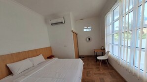 A hotel room with a large bed, a desk, and a chair. There is a window with blinds and an air conditioning unit on the wall. - Hotel O Safira Guest House Danau Ranau (Muaradua)