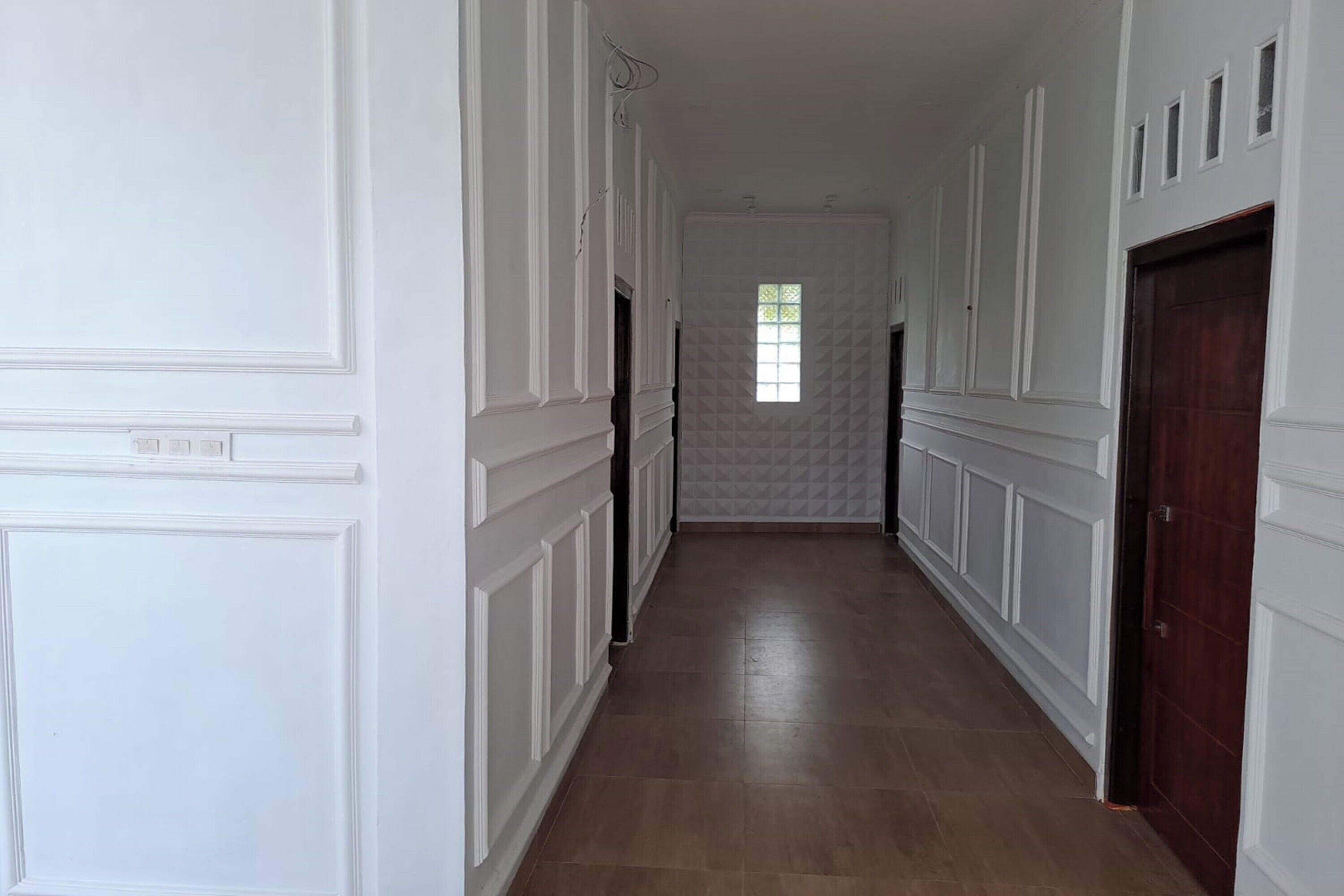 Un couloir avec des lambris blancs, un plancher en bois et une porte sur le côté droit.