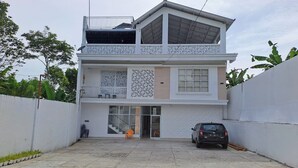 A two-story building with a balcony, a car parked in front, and a gate. - Hotel O Safira Guest House Danau Ranau (Muaradua)