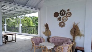 A covered patio area with wicker furniture, a table, and decorative wall art. - Hotel O Safira Guest House Danau Ranau (Muaradua)