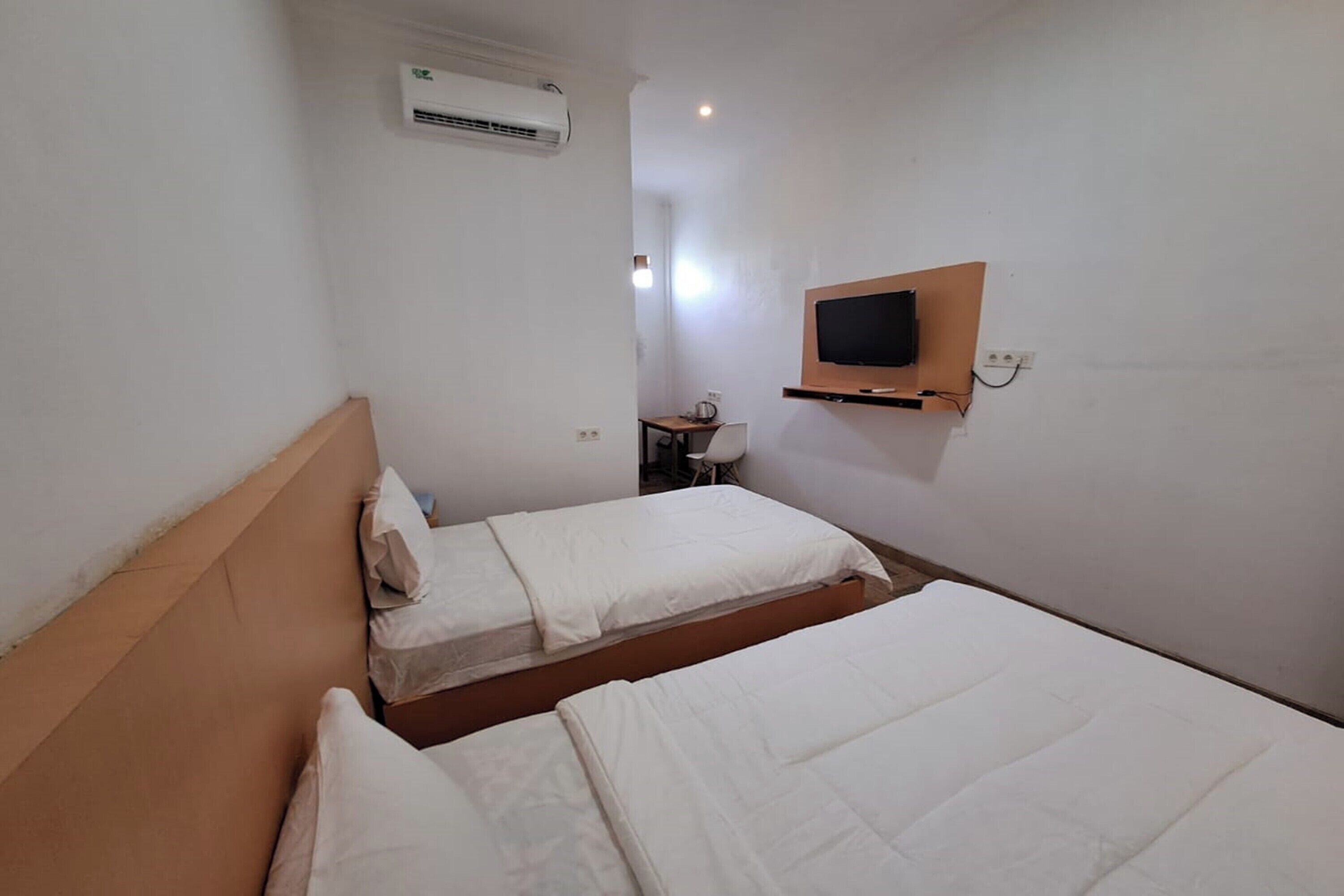 A hotel room with two beds, an air conditioning unit, a desk with a chair, and a mounted TV.