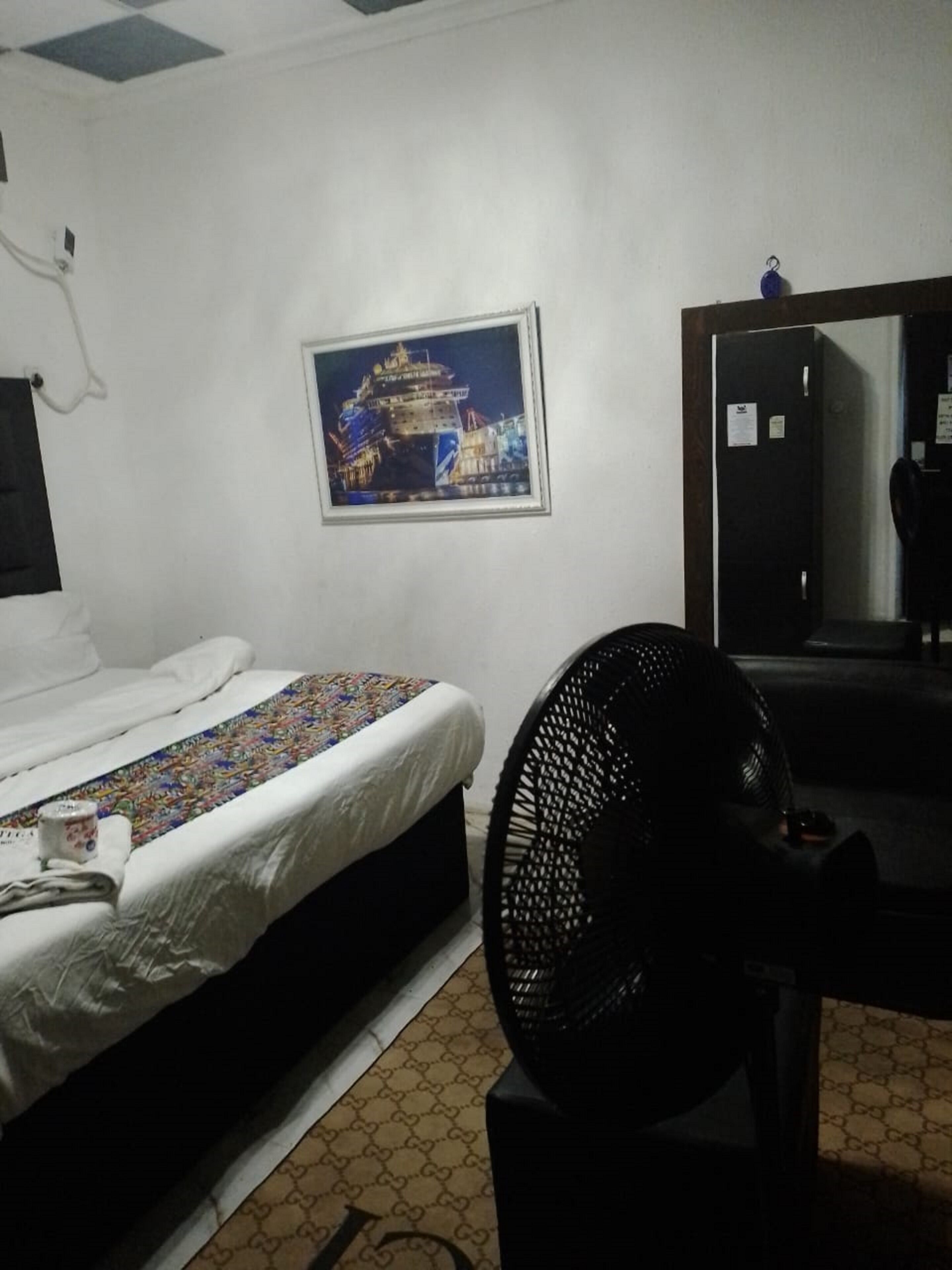A hotel room with a bed, a fan, a framed picture on the wall, and a mirror.