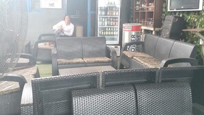 A covered outdoor seating area with wicker furniture, a fan, and a refrigerator stocked with beverages. - Tega Suites Ikeja (Lagos)