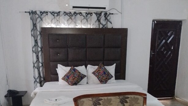 A bedroom with a bed, two floral-patterned armchairs, a small table, and a dark door. - Tega Suites Ikeja (Lagos)