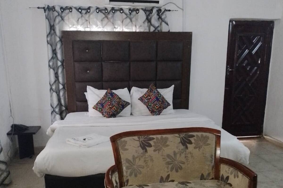 A bedroom with a bed, two floral-patterned armchairs, a small table, and a dark door.