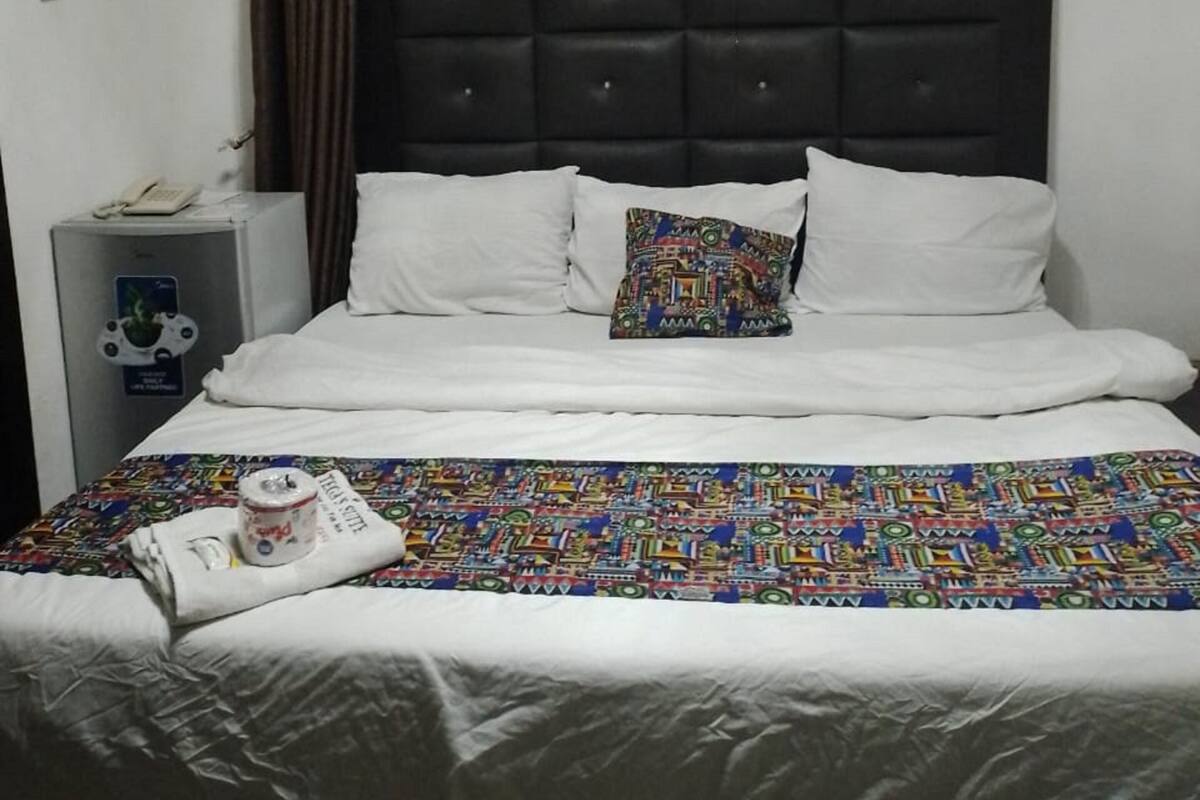 A hotel room with a bed, a bedside table, an air conditioning unit, and a curtain.
