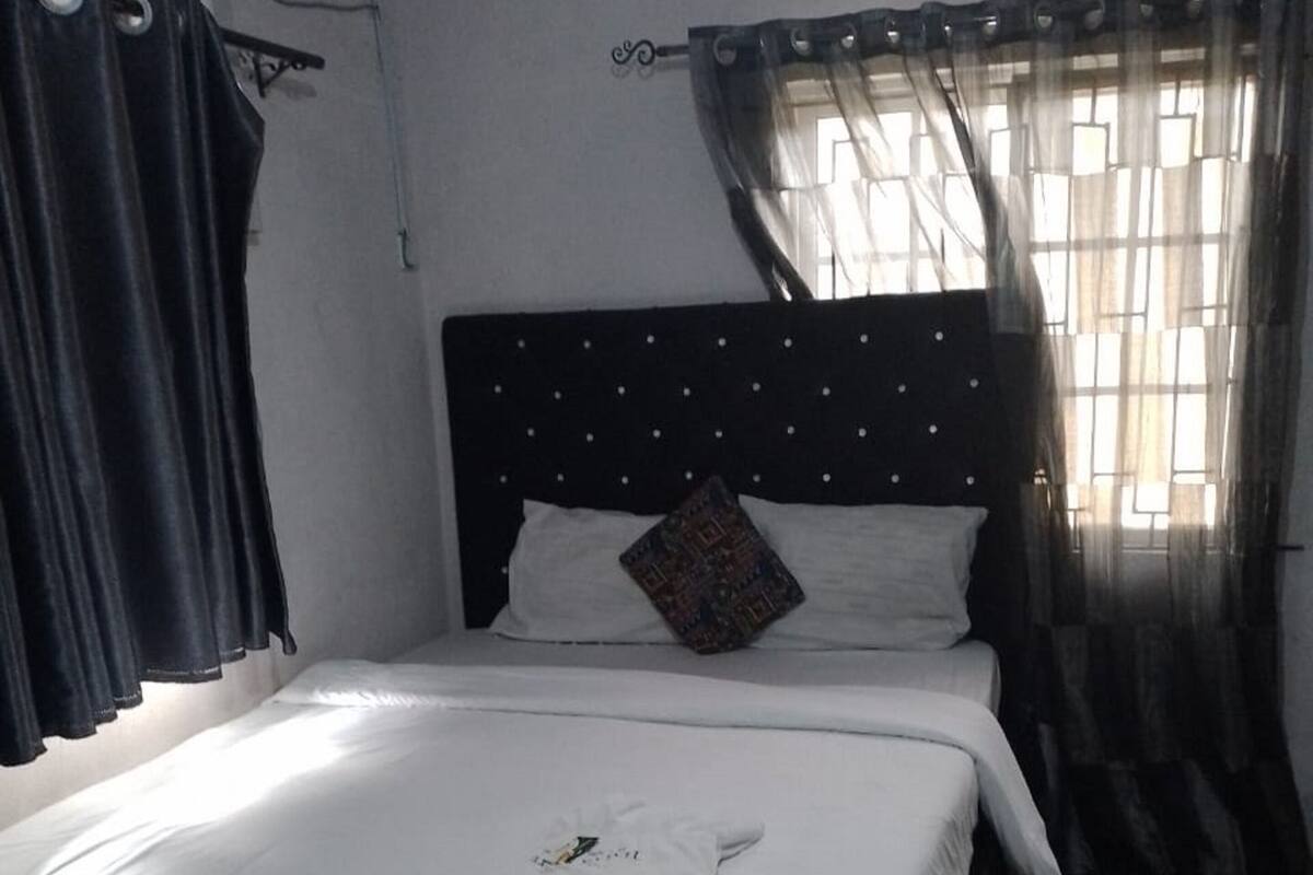 A neatly made bed with white linens, a black headboard with a pattern, and a single decorative pillow.